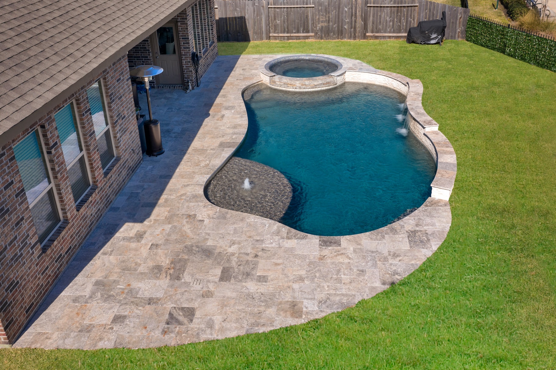 Freeform pool with raised round spa, tanning ledge, and travertine Versailles decking