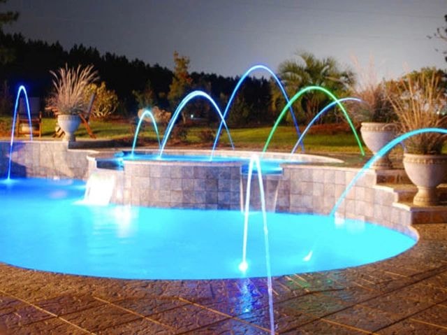 Color-changing LED deck jets illuminated at night over a custom pool