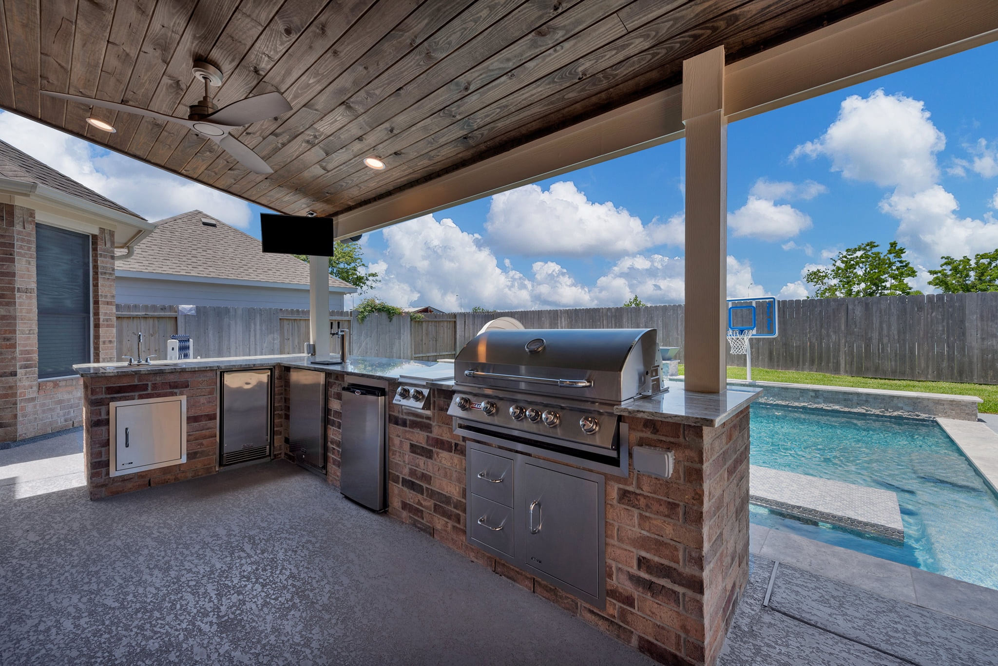 Covered outdoor kitchen with built-in grill, stone counters, and pool view