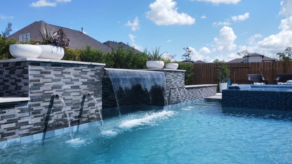 Custom pool with glass tile sheer descent water wall and raised spillover spa